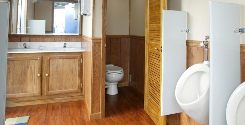 interior view of a mens bathroom trailer with two sinks, a private toilet and two urinals