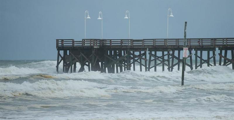 The Daytona Beach Pier with white lampposts extending into a stormy sea with choppy waves under a cloudy sky