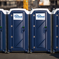A row of blue portable toilets with "United Site Services" logo lined up outdoors in a daytime setting
