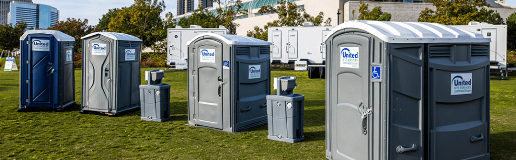 Row of portable toilets and restroom trailers lined up in a grassy area behind the San Diego Convention Center, with hand sanitizer stations positioned next to each unit