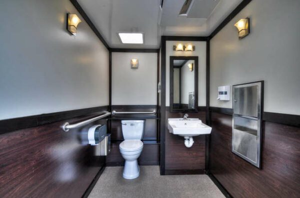 ADA-compliant restroom with dark wooden floors, white walls, a white toilet to the left, a sink to the right, and a mirror in the center