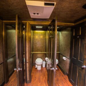 Interior of USS's Platinum Series Restroom Trailer stalls, featuring a wooden floor, brown doors, and a brown brushed wallpaper