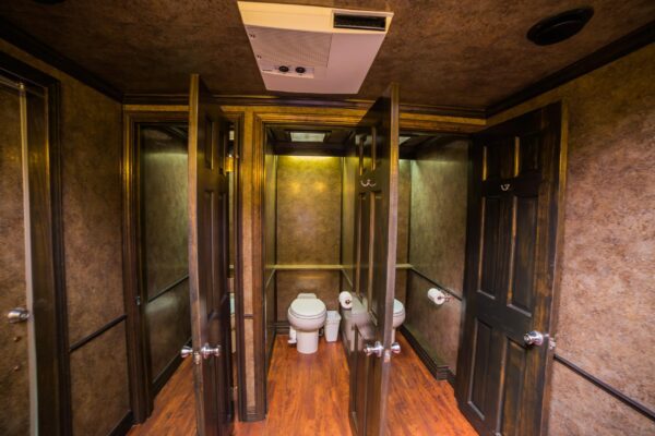 Interior of USS's Platinum Series Restroom Trailer stalls, featuring a wooden floor, brown doors, and a brown brushed wallpaper