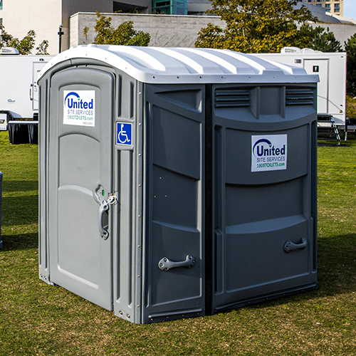 A gray ada portable toilet with a white roof and handicap accessibility logo, located outdoors in a grassy area