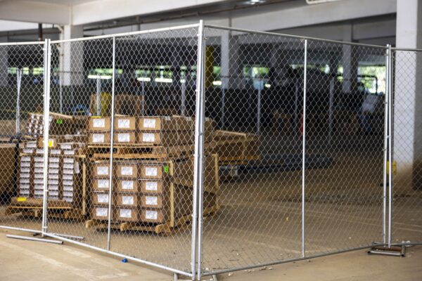A metal fence enclosing a warehouse space with wooden pallets and crates visible inside, in an industrial setting with soft lighting