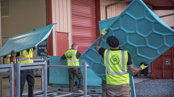 Workers in high visibility vests move large blue honeycomb panels at a warehouse to build Hydroflow showers.