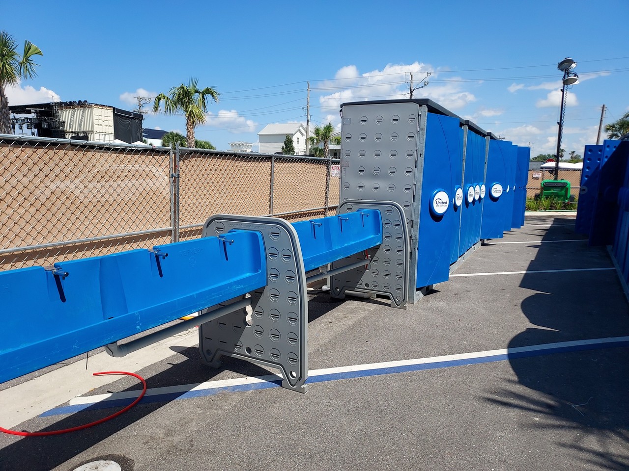 Row of blue Hydroflow sinks connected to portable restrooms in a parking lot with palm trees and a blue sky in the background