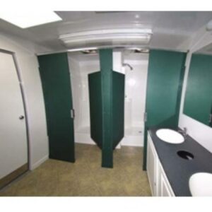 Interior of a portable shower trailer with white walls, green stall doors, and two sinks against a white countertop
